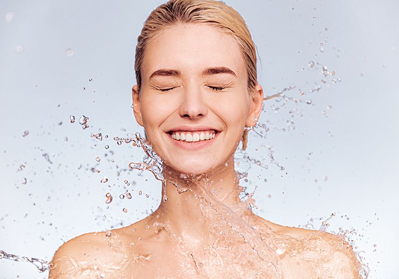 Rostro de mujer con la piel limpia que le está salpicando el agua.